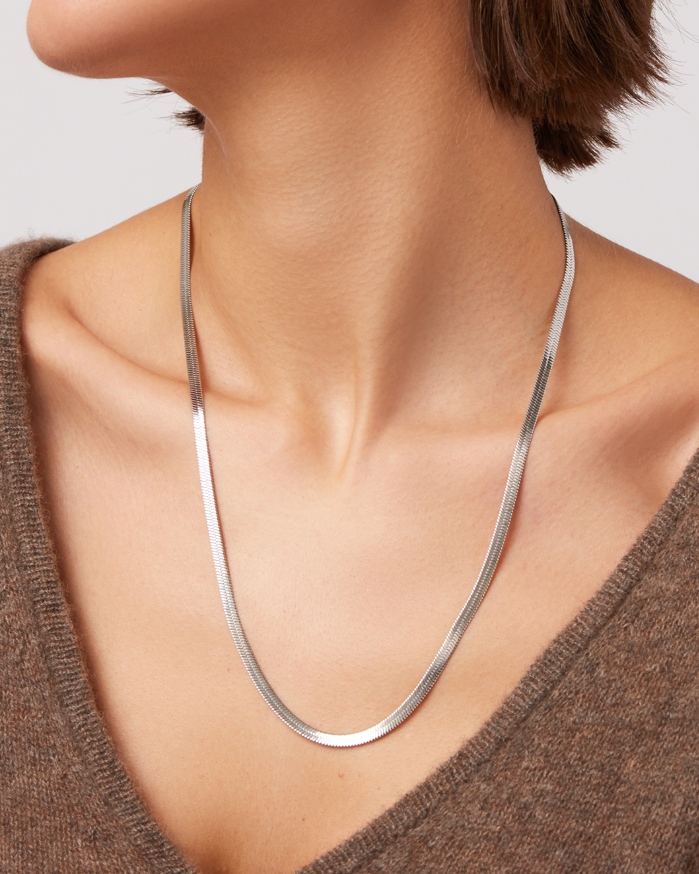 Portrait of a woman with braided hair, silver earrings, and a beige top.